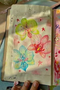 an open notebook with flowers and stars on it, next to a person's hand