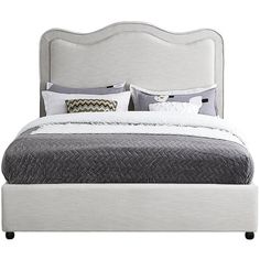 a white bed with grey and white pillows on top of it, next to a night stand