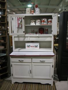 an old fashioned white kitchen cabinet with red and green trim on the top, in a store