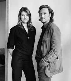 a man and woman standing next to each other in front of a white wall, posing for the camera