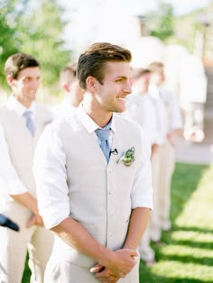 a man in a white suit and tie standing next to other men