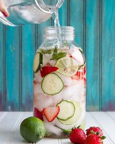 a mason jar filled with cucumbers, strawberries and limes sitting on a table