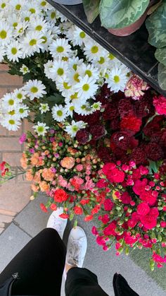 a person standing in front of a bunch of flowers with their feet on the ground