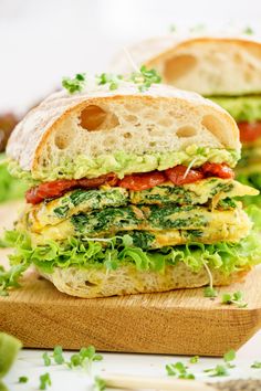 a sandwich with lettuce, tomato and avocado is on a cutting board