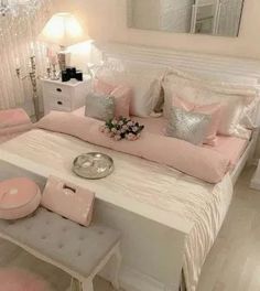 a white bed with pink and silver pillows on top of it next to a mirror