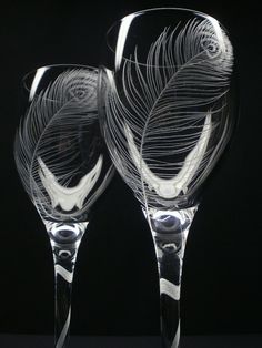 two wine glasses with feathers on them sitting side by side in front of a black background