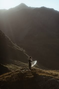 a man standing on top of a grass covered hillside holding a white frisbee