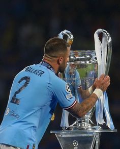 a soccer player holding the trophy in front of his face and looking down at it