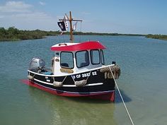 a red and white boat floating on top of a lake next to a sandy beach