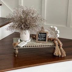 a wooden table topped with a white vase filled with flowers and a chalkboard sign