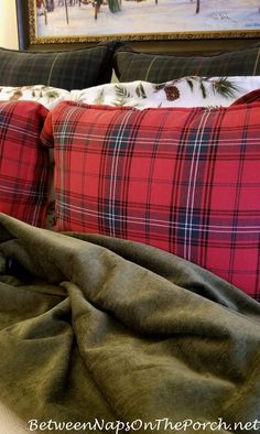 a bed with red and green plaid pillows on it's headboard next to a painting