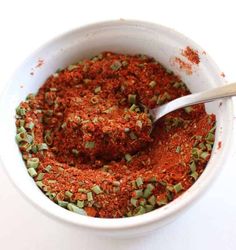 a white bowl filled with red seasoning and sprinkled green pepper flakes