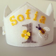 a white felt crown with yellow letters and bees on it