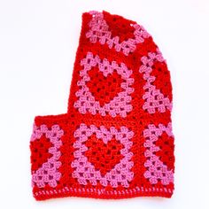 a crocheted red and pink hat with hearts on it sitting on a white surface