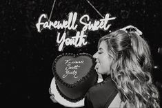 a woman holding a heart shaped cake in front of a sign that says farewell sweet youth