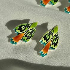 three green and orange butterfly shaped brooches on a white cloth with shadow from the back