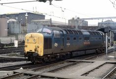 a yellow and black train is on the tracks near some buildings in an industrial area