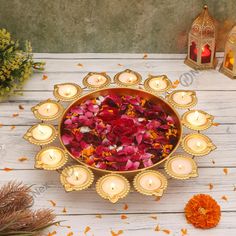 a bowl filled with flowers and candles on top of a white wooden table next to orange flowers