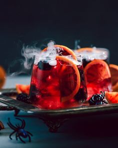 two glasses filled with red liquid and orange slices on a metal tray next to spider webs