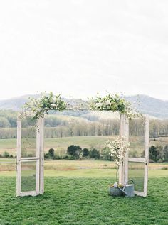 an outdoor ceremony setup with white flowers and greenery on the grass in front of mountains