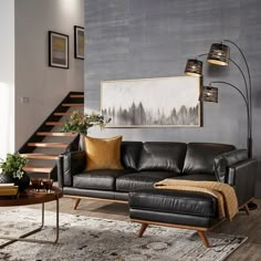 a living room with black leather couches and a wooden coffee table in front of a stair case