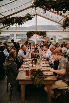 a group of people sitting around a wooden table eating food under a tented area