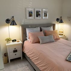 a bed with pink sheets and pillows in a bedroom next to two pictures on the wall