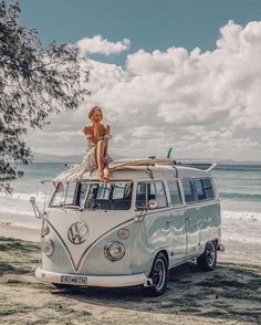 a woman sitting on top of an old vw camper van at the beach