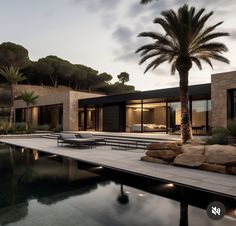 a large pool surrounded by palm trees next to a house with glass doors and windows