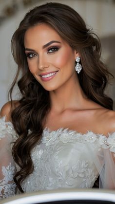 a woman with long hair wearing a white dress and diamond earrings smiling at the camera