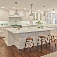 a large white kitchen with two stools in front of the island and an oven