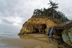 a rocky beach with a small waterfall coming out of the cliff into the water and trees in the background