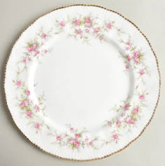 a white plate with pink flowers on the side and gold trimmings around the edge