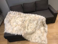 a large white fur rug sitting on top of a wooden floor next to a couch