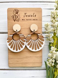 a pair of wooden earrings sitting on top of a wooden board next to flowers and a plant