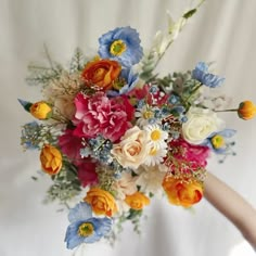 a bouquet of colorful flowers is held by a woman's hand in front of a white backdrop