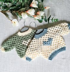 two crocheted sweaters sitting on top of a table next to some flowers