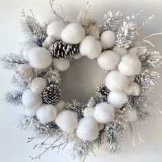 a white christmas wreath with pine cones and snow balls on the front, surrounded by evergreen branches