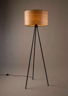 a floor lamp with a wooden shade on it's base and a black metal tripod leg