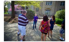 a group of people standing in front of a building with trees and flowers on the ground