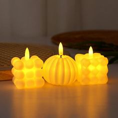 three lit candles sitting next to each other on top of a table with an object in the background