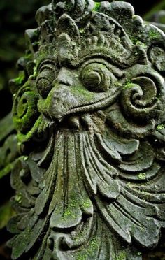 an old statue with moss growing on it's face and head in the background