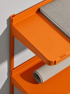 an orange desk with a laptop on top and a roll of paper under the edge