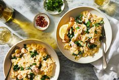 two bowls of pasta with spinach and salmon on a marble countertop next to wine glasses