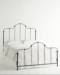 an iron bed frame with white linens and pillows on the headboard, against a plain white wall