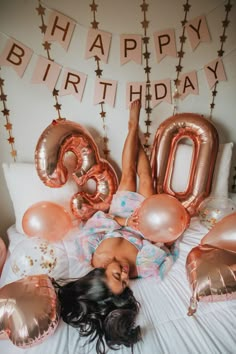 a woman laying on top of a bed surrounded by balloons and streamers in the shape of numbers