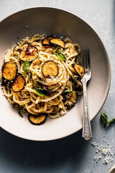 pasta with eggplant and parmesan cheese in a white bowl next to a fork