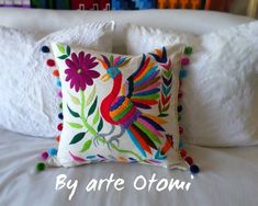 a decorative pillow on top of a bed with white linens and pom poms