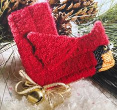 a red knitted bird ornament sitting on top of snow next to pine cones