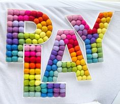 the letters are made out of different colored felt balls and placed next to each other